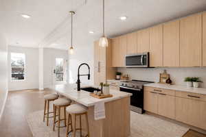 Kitchen featuring light wood finish cabinetry, stainless steel appliances, modern cabinets, an island with sink, and a textured ceiling