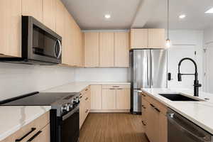 Kitchen featuring stainless steel appliances, light wood finish cabinets, light stone countertops, and decorative light fixtures