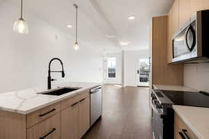 Kitchen with light wood finish cabinets, stainless steel appliances, modern cabinets, an island with sink, and a textured ceiling