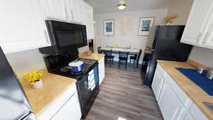 Kitchen with black appliances, white cabinets, dark wood-type flooring, and light countertops