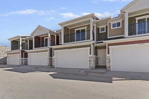 View of front of house featuring a balcony, stone siding, a garage, board and batten siding, and concrete driveway
