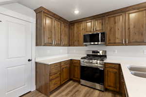 Kitchen with stainless steel appliances, wood finish cabinetry, light wood-type flooring, and light stone countertops