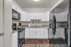 Kitchen with black appliances, light stone countertops, white cabinetry, dark wood finished floors, and a textured ceiling