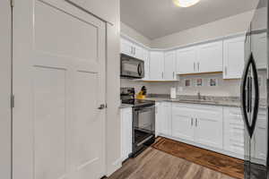 Kitchen featuring black appliances, light stone countertops, white cabinets, a textured ceiling, and dark wood-type flooring
