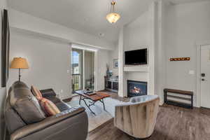 Living room featuring lofted ceiling, dark wood-type flooring, and a glass covered fireplace