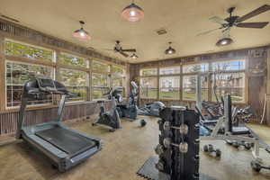 Workout area featuring a ceiling fan, wood walls, and a textured ceiling