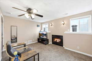 Living area featuring carpet flooring, a glass covered fireplace, and ceiling fan