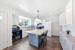 Kitchen with white appliances, a center island, light countertops, hanging light fixtures, and white cabinets