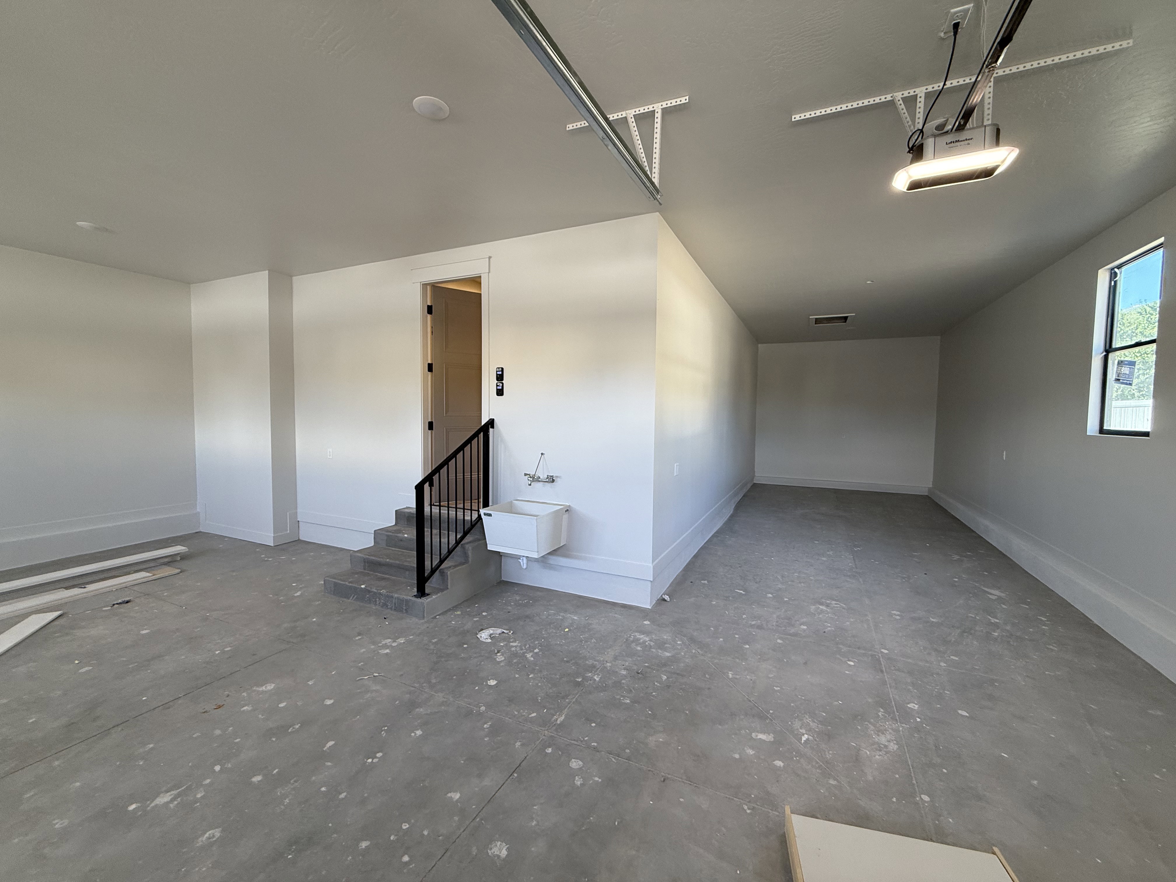 Spacious garage with concrete flooring, utility sink, and internal access staircase with a black metal handrail