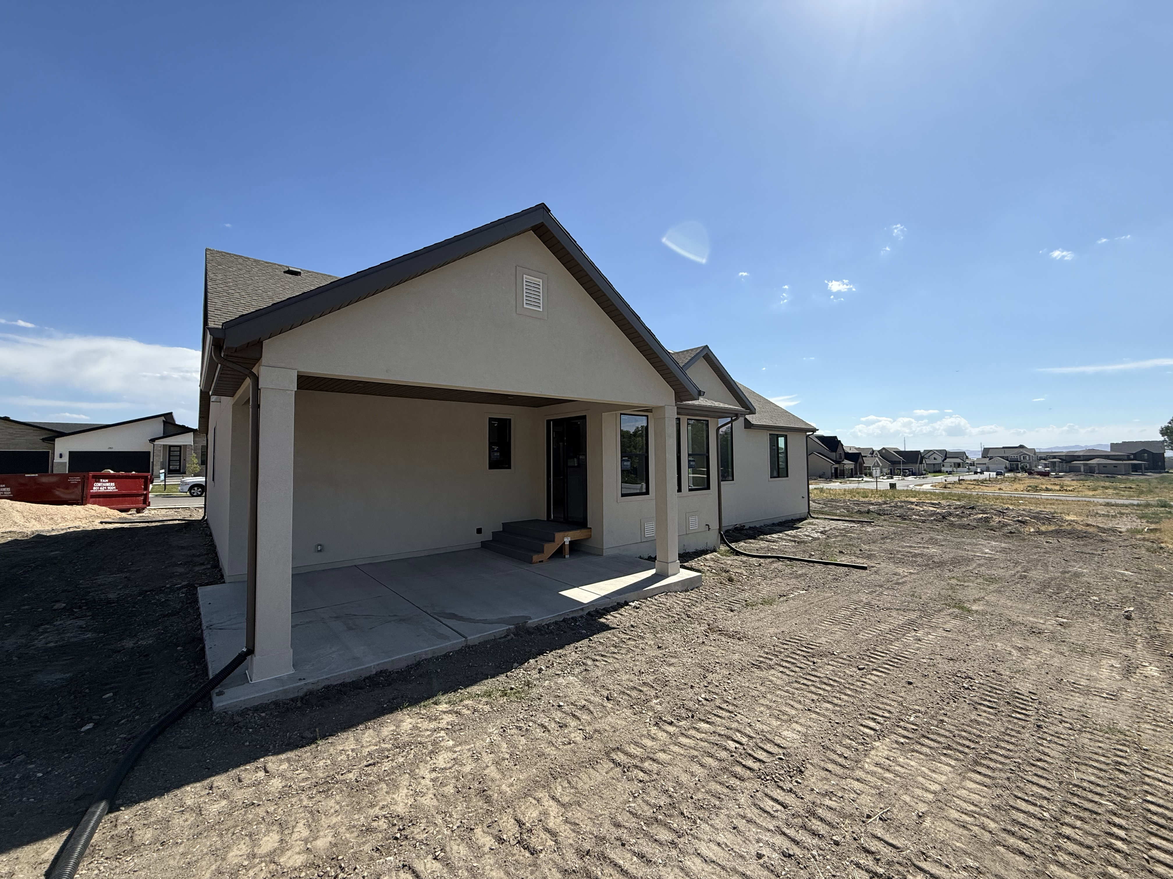 Rear exterior featuring a covered patio with concrete flooring, stucco siding, a dark roof, and a visible downspout