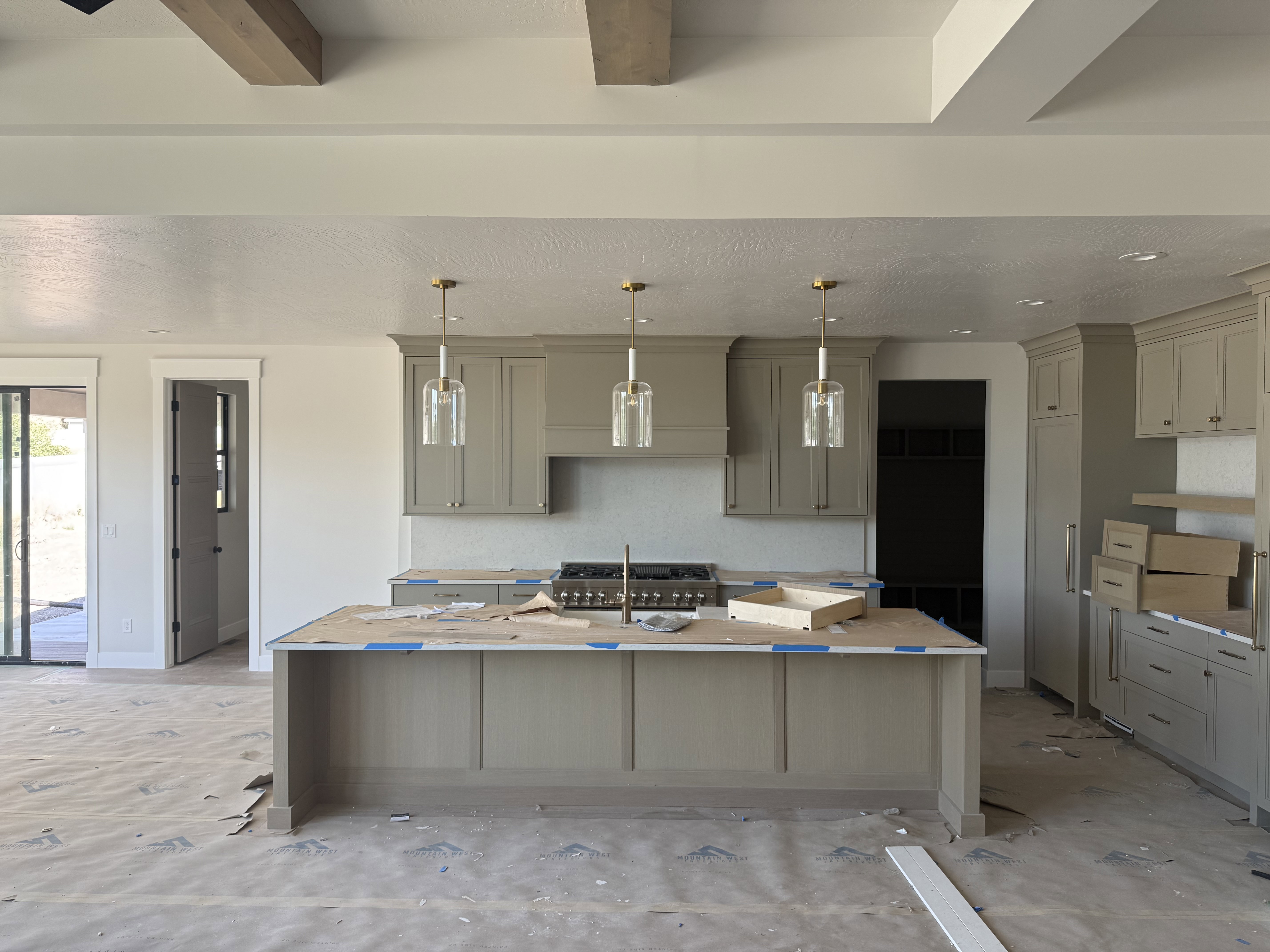 Spacious kitchen featuring an expansive center island, a full suite of cabinetry, exposed wood ceiling beams, and contemporary pendant lighting fixtures