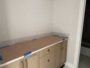 Light wood-finish vanity with gold-tone hardware, a light-colored countertop, and a matching backsplash