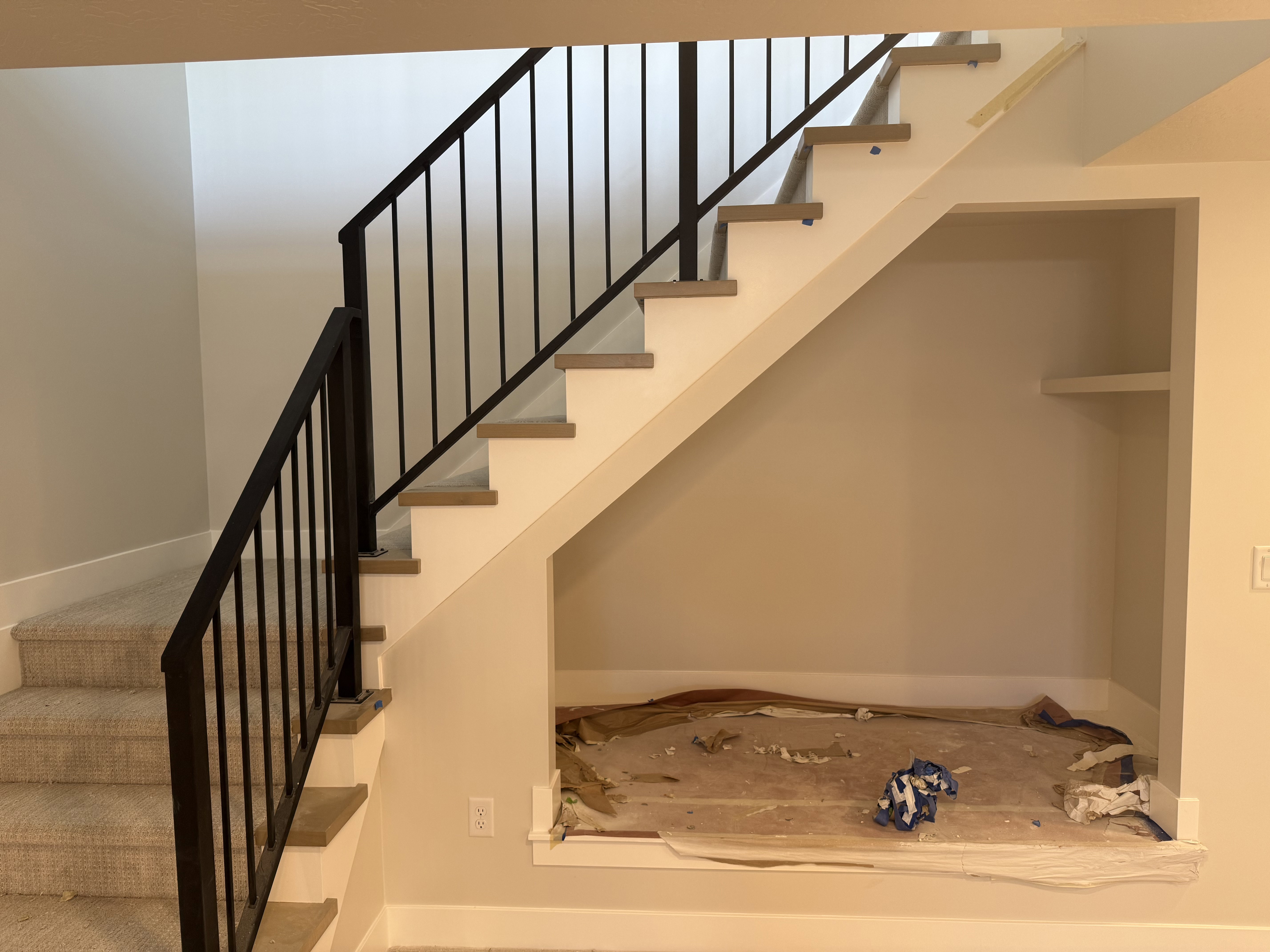 Staircase featuring dark metal balusters, light wood-finish treads, and plush carpeted risers