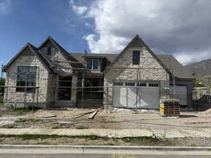 View of front of home with stone siding, a garage, and a shingled roof