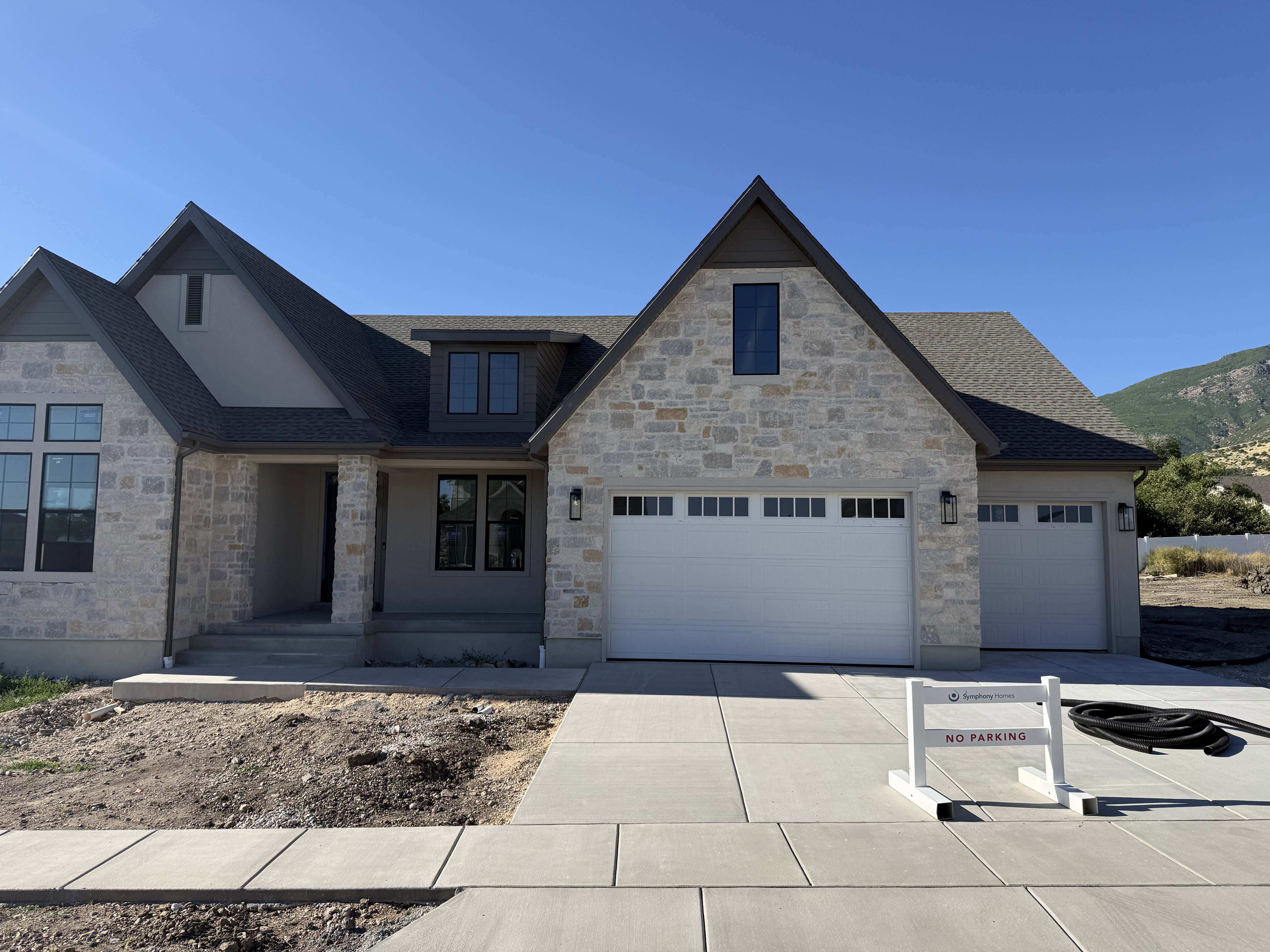 Stone and stucco exterior featuring multiple gables, a two-car garage, a single-car garage, and a concrete driveway