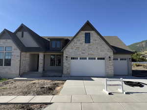 Stone and stucco exterior featuring multiple gables, a two-car garage, a single-car garage, and a concrete driveway