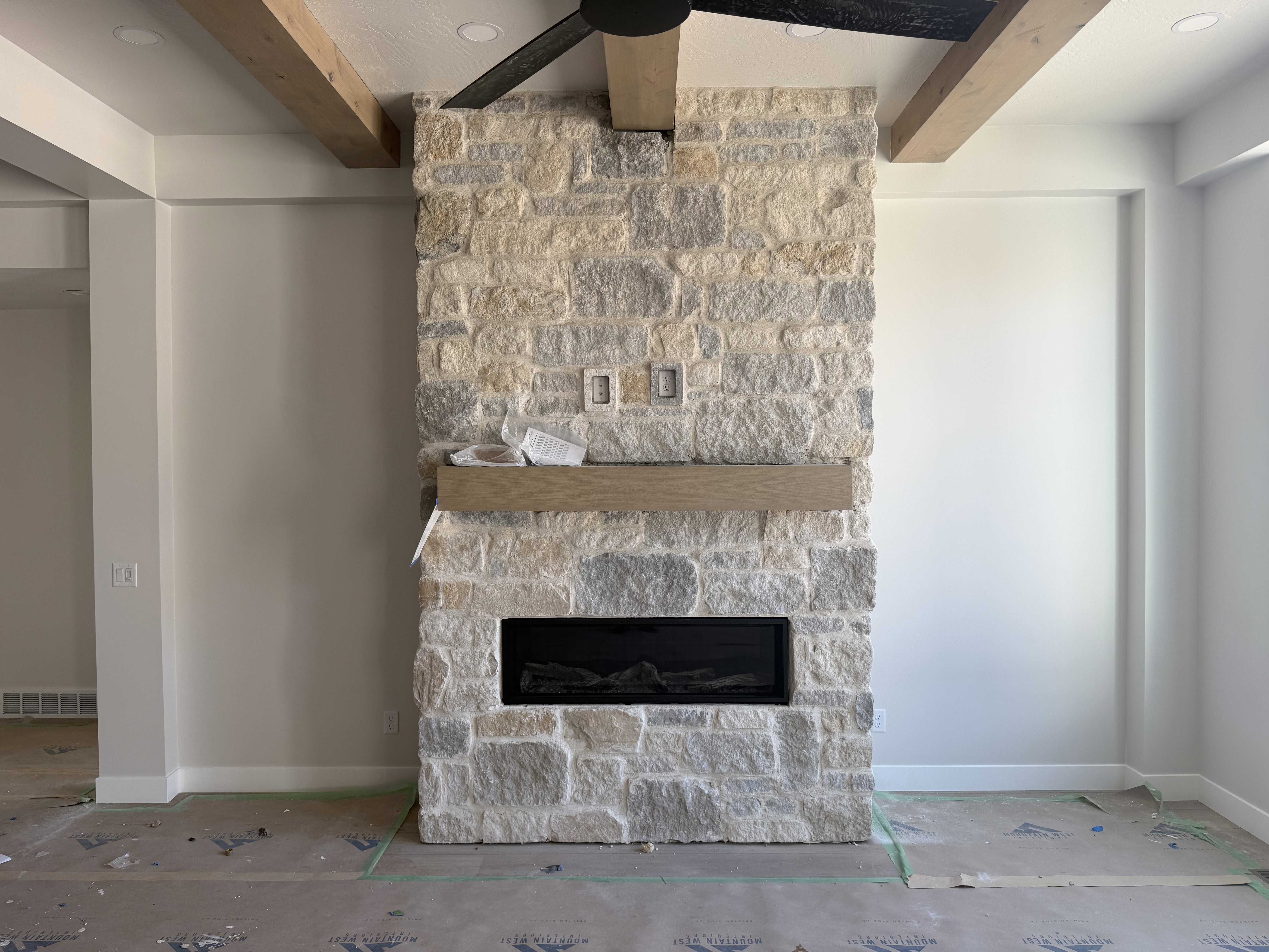 Stone fireplace featuring a linear electric insert and a natural wood mantel