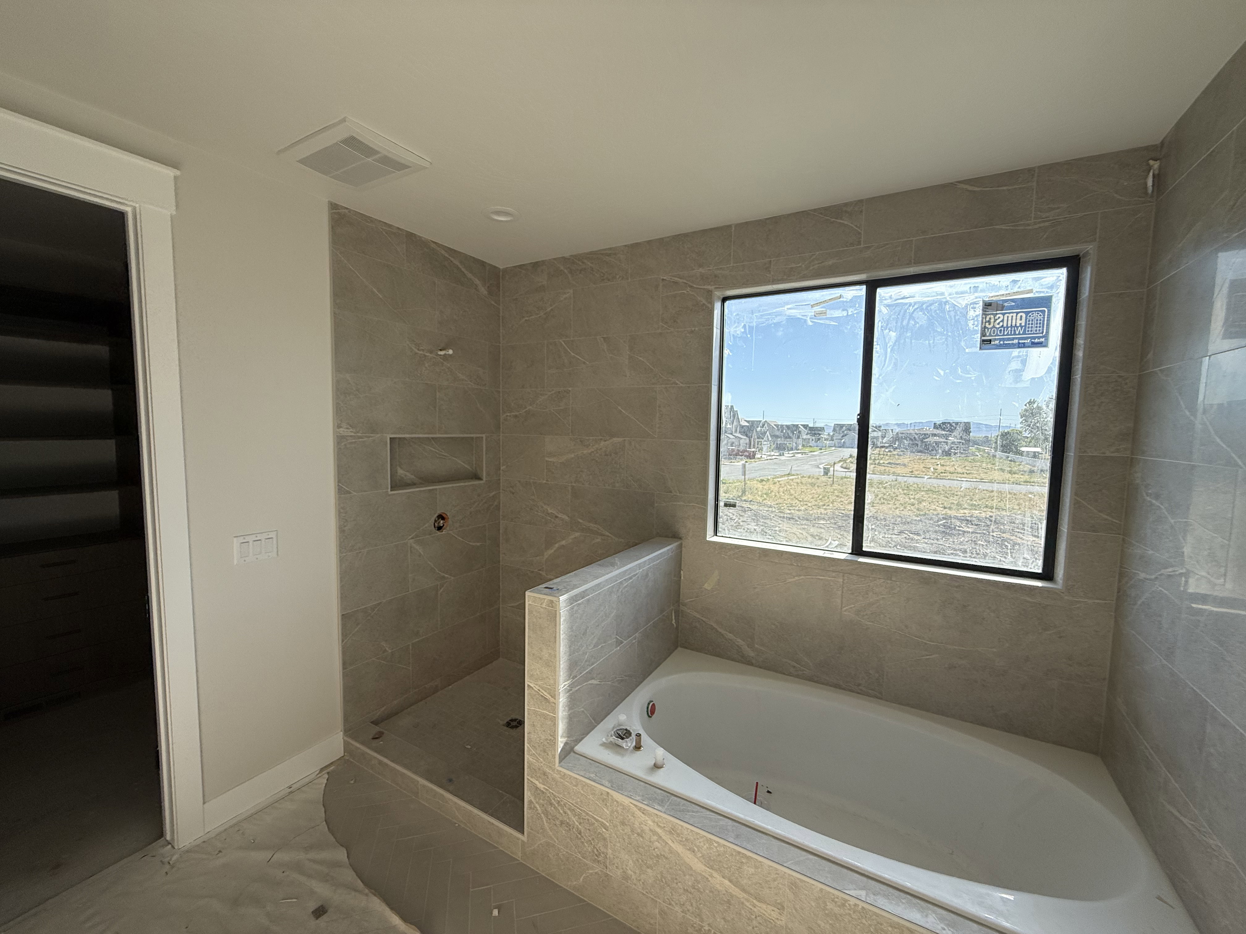 Bathroom featuring a built-in soaking tub, tiled shower with integrated niche, and a large window