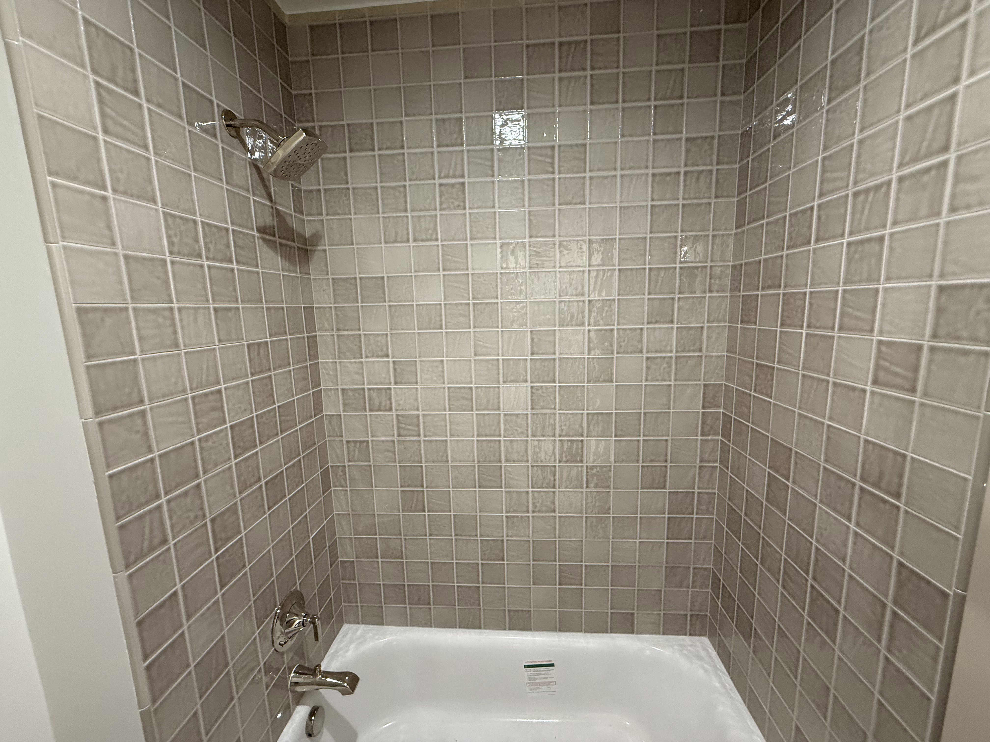 Bathtub with light gray mosaic tile surround and polished chrome fixtures