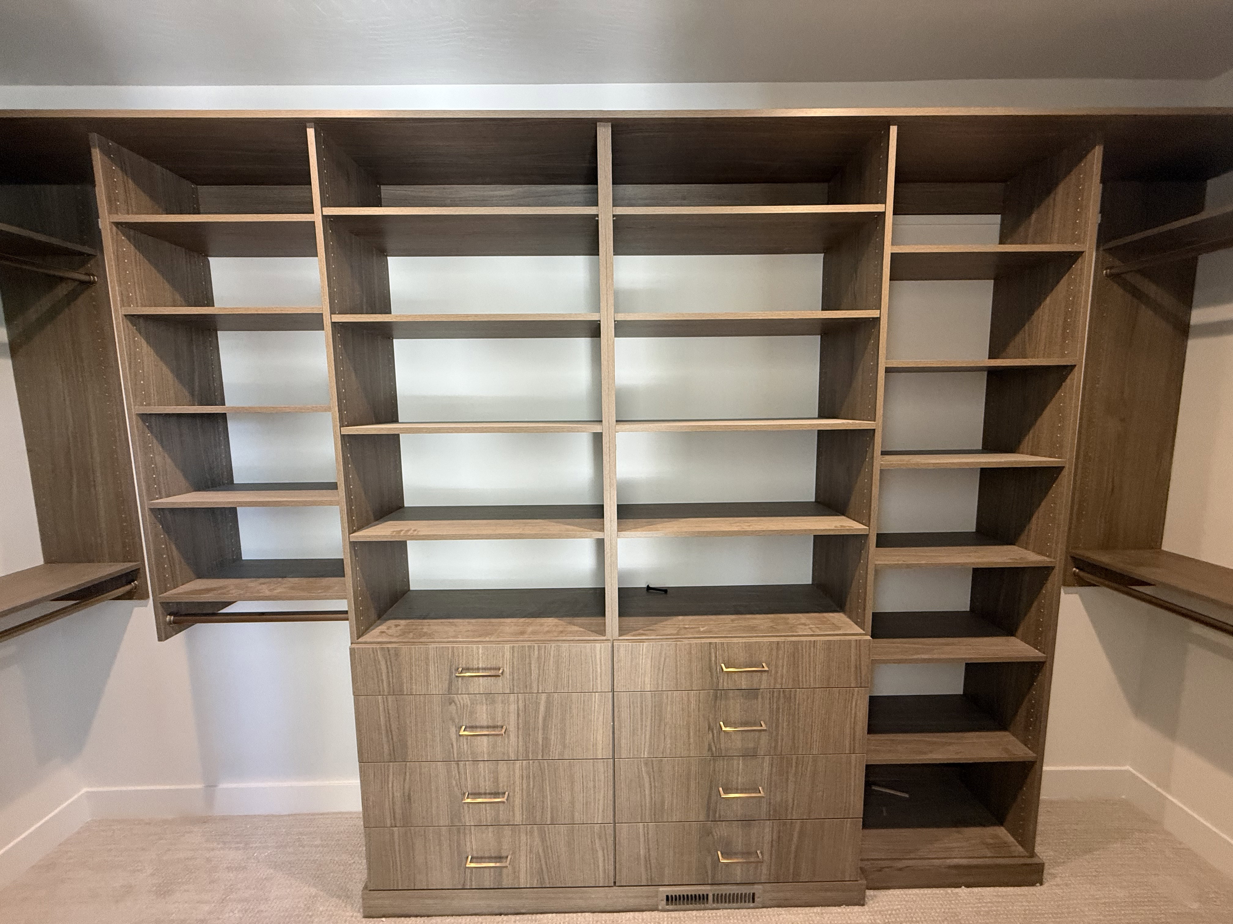 Custom closet system featuring wood-finish cabinetry, integrated shelving, and multiple storage drawers with gold-tone hardware