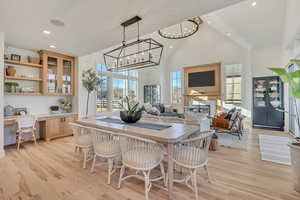 Dining room with built in study area, a glass covered fireplace, light wood-style flooring, healthy amount of natural light, and lofted ceiling