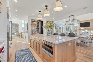 Kitchen with a center island, light stone counters, light wood-style floors, light wood finish cabinetry, and decorative light fixtures