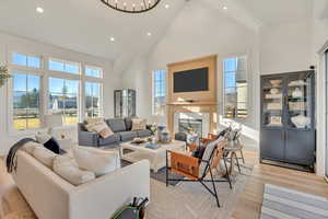 Living room featuring a glass covered fireplace, a high ceiling, light wood-type flooring, and suspended lighting