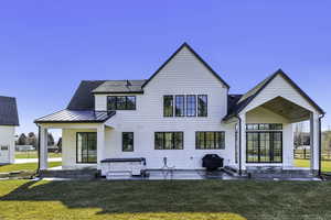 Rear view of house featuring a patio, a lawn, and a standing seam roof