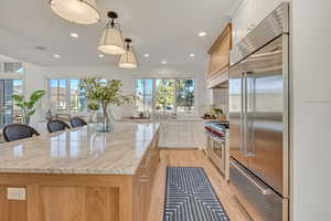Kitchen featuring backsplash, premium appliances, dual tone cabinetry, light stone counters, and a spacious island