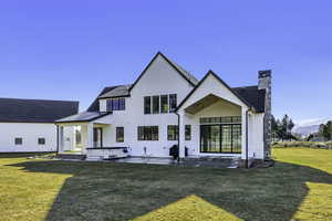 Rear view of house featuring a chimney, a patio, a lawn, and a standing seam roof