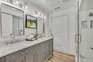 Full bathroom with a marble finish shower, double vanity, and light wood-style flooring