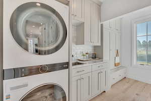 Laundry room with light wood-style floors, cabinet space, and stacked washing machine and dryer