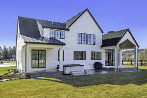 Rear view of house featuring a patio, a hot tub, a yard, and a shingled roof