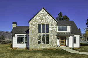 View of front facade with stone siding, a standing seam roof, a chimney, roof with shingles, and a porch