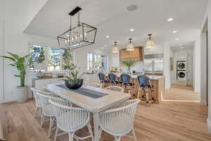 Dining space with light wood-style flooring, stacked washer and clothes dryer, and suspended lighting