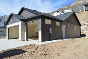 View of property exterior with board and batten siding, a mountain view, roof with shingles, and stone siding