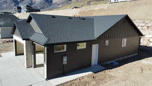 View of side of property featuring a shingled roof, board and batten siding, a mountain view, and stone siding