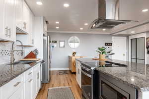 Kitchen featuring stainless steel appliances, island range hood, dark stone countertops, white cabinets, and crown molding