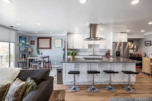 Kitchen with white cabinetry, dark stone counters, island range hood, open floor plan, and crown molding