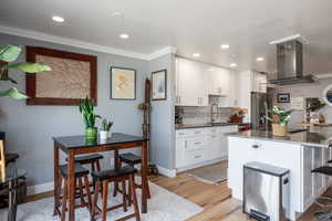 Kitchen featuring dark stone countertops, island range hood, light wood-type flooring, white cabinets, and ornamental molding
