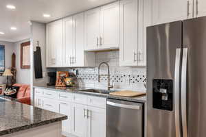 Kitchen with stainless steel appliances, white cabinets, dark stone countertops, ornamental molding, and recessed lighting