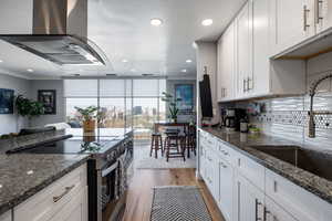 Kitchen with dark stone counters, stainless steel electric stove, white cabinets, extractor fan, and recessed lighting