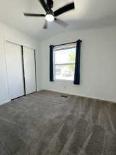 Unfurnished bedroom featuring dark carpet, vaulted ceiling, ceiling fan, and a closet