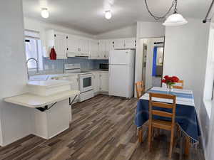 Kitchen with light countertops, white appliances, lofted ceiling, white cabinets, and a peninsula