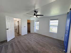 Unfurnished bedroom featuring a spacious closet, dark colored carpet, a barn door, ceiling fan, and a heating unit