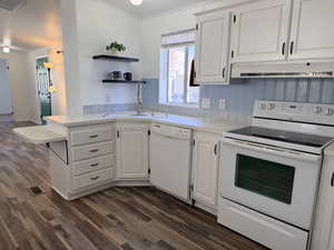 Kitchen featuring white appliances, light countertops, a peninsula, white cabinetry, and dark wood-style flooring
