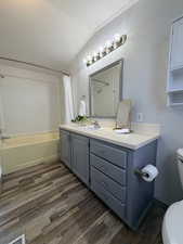 Bathroom featuring a textured wall, vanity, shower / tub combo, dark wood-type flooring, and vaulted ceiling