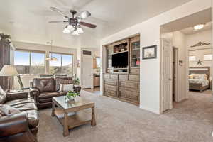 Living area with light carpet, ceiling fan, and a chandelier