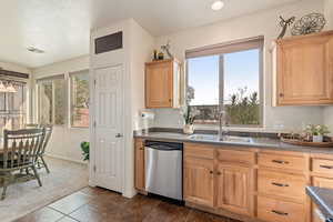 Kitchen featuring dark countertops, dishwasher, healthy amount of natural light, and light wood finish cabinets