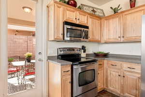 Kitchen featuring light wood finish cabinetry, stainless steel appliances, and dark countertops